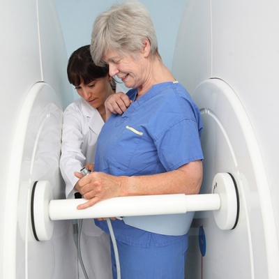 A patient stands between the sections of the upright open MRI while the technician configures the machine.